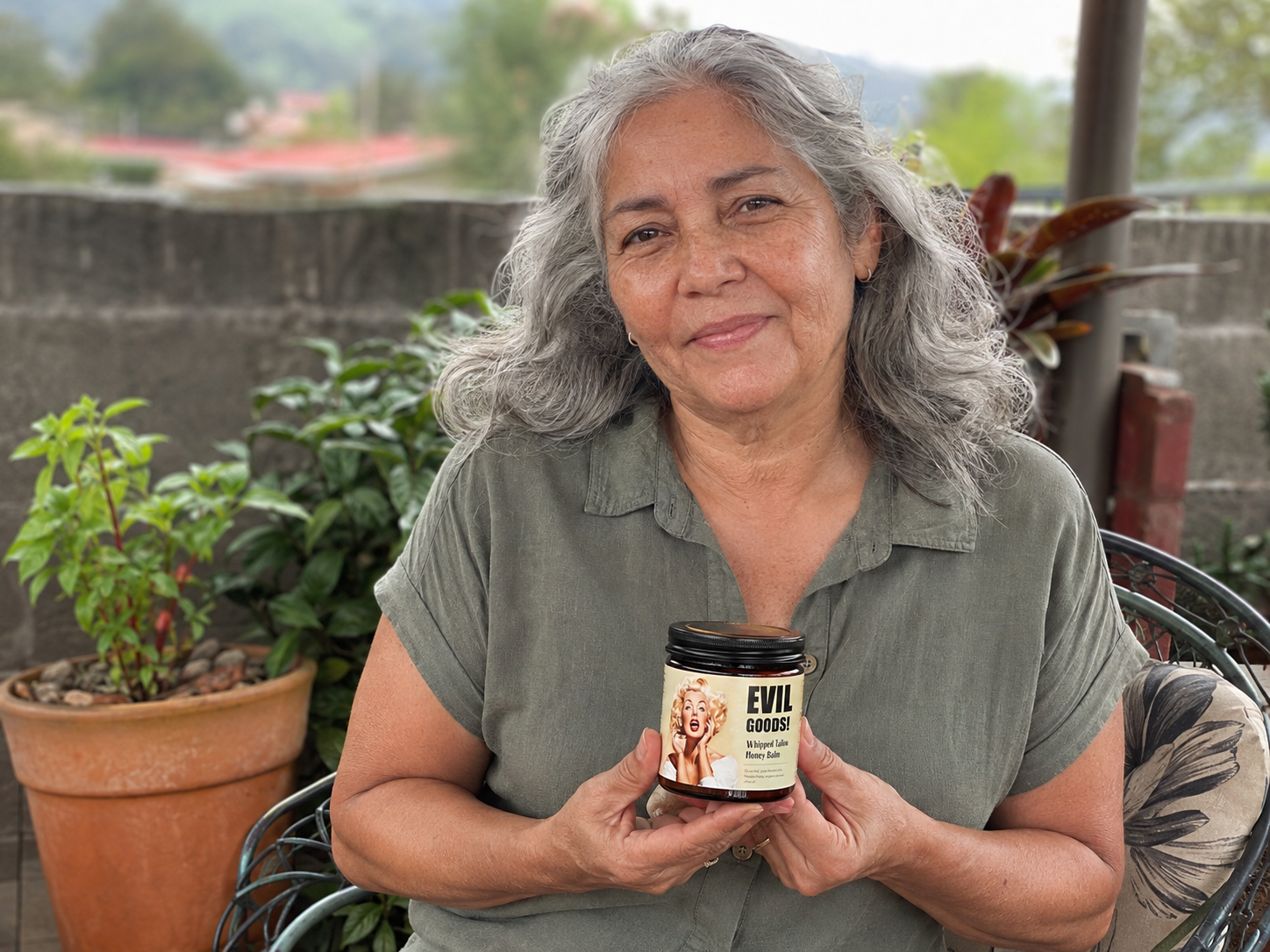 Mujer costarricense de cabello canoso mostrando Evil Goods en un patio
